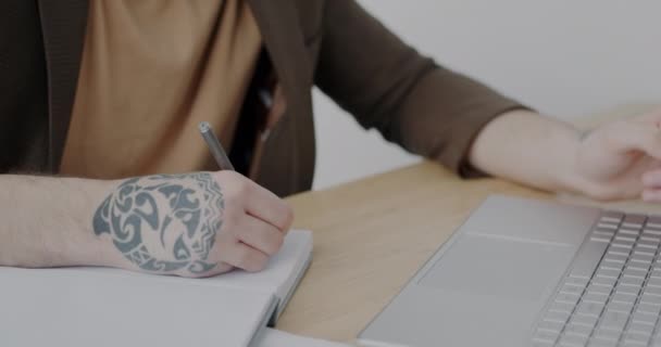 ノートにタトゥーを書き ビジネスマンが一人でデスクで働いている間 オフィスでノートパソコンを使用して男性の手のクローズアップ 人々と個々のスタイルの概念 — ストック動画
