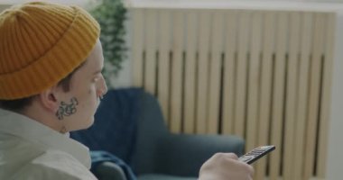 Benzersiz bir dövmesi olan neşeli bir insan ve dairede televizyon seyrederek atıştırmalık bir şeyler yiyor. Bireysellik ve boş zaman aktivite kavramı.