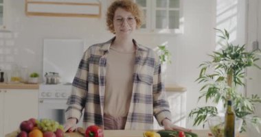 Mutfakta durup kameraya gülümseyen güzel bir kadının yavaş çekim portresi. Rahat iç çamaşırı ve gözlük takan bir bayan..