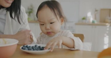 Anne çocukla konuşurken, tatlı küçük kız böğürtlen yiyor ve mutfakta sevgisini dile getiriyor. Aile ve mutluluk kavramı.