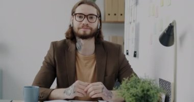 İşletme sahibi, modern teknolojiyi kullanarak internet üzerinden video görüşmesi yapıyor. Dövmeli ve son moda saç stili olan genç adam kameraya bakıyor ve el kol hareketi yapıyor..