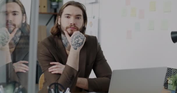 現代オフィスで机の上にタトゥーのある若い男のスローモーションポートレート スタイリッシュな服に座ってカメラを見て創造的なビジネスマン — ストック動画