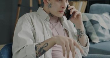 Cep telefonuyla konuşan ve evde gülen neşeli bir gencin portresi. Dövmeli ve piercingli biri sohbetten zevk alıyor..