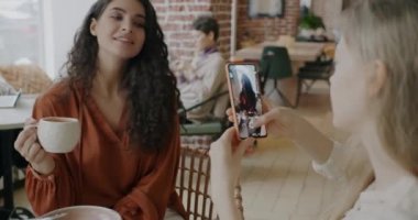 Arkadaş modern kafede fotoğraf çekerken akıllı telefon kamerasına poz veren neşeli öğrenci portresi. Teknoloji ve fotoğraf konsepti.