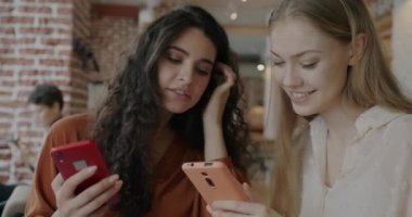 Akıllı telefon kullanan genç bir bayanın portresi kafede gülen bir arkadaşına ekranı gösteriyor. Modern teknoloji ve sosyal medya kavramı.