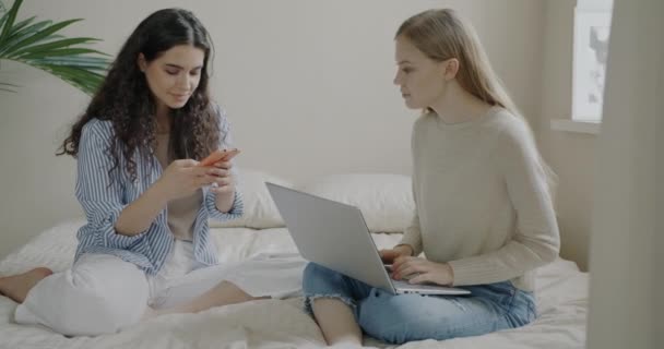 Щасливі Молоді Жінки Друзі Використовують Ноутбук Смартфон Розмовляють Сидячи Ліжку — стокове відео