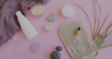 Pembe masadaki modern organik spa ürünlerinin yakınlaştırılması ve kadın elinin bir şişe kozmetik yağı koyması. Sağlık ve vücut bakımı kavramı.