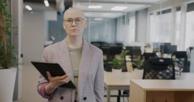 İşkadını portresi ofiste tablet kullanarak yürüyor ekrana dokunuyor ve kameraya bakıyor. Modern teknoloji ve profesyonel işgal kavramı.
