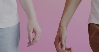Erkek ve kadının el ele tutuşup pembe arka planda sevgisini ve desteğini ifade ettiği yakın plan. Romantik ilişki ve birliktelik kavramı.
