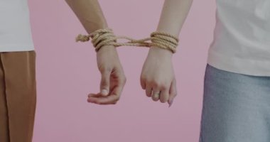 Kadın ve erkek ellerini yakın plan pembe arkaplandan ayırmaya çalışıyorlar. İlişki sorunları ve insanların kavramı.
