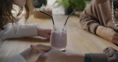 Kız ve erkeğin bir bardaktan milkshake içerken ve kafede romantik bir randevu sırasında el ele tutuşurken. İlişki ve flört kavramı.