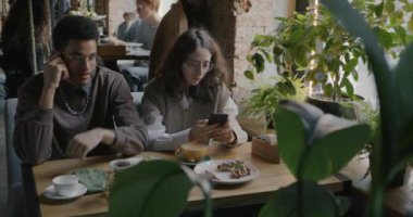 Kafkasyalı kız arkadaş kafede akıllı telefon mesajları kullanırken Afro-Amerikalı adam cep telefonuyla konuşuyor. İnsanlar ve iletişim konsepti.