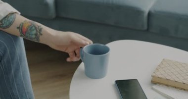 Moda kıyafetli, fincandan çay içen ve evde televizyon izleyen yaratıcı genç adamın portresi. İçecek ve boş zaman etkinliği kavramı.