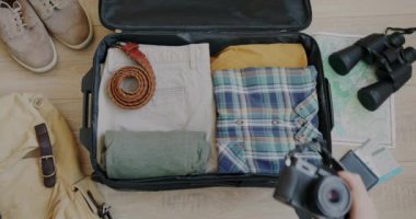 El çantasının yakın çekimi fotoğraf makinesini çantaya koyup tatile hazırlanıyor. Turizm objeleri ve bagaj hazırlığı düzlüğü.