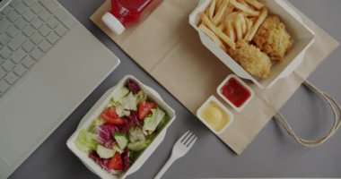 Gri arka planda dizüstü bilgisayarın yanında hazır yemek torbası olan konteynırların üst görüntüsü. Öğle yemeği ve ofis yemeği konsepti..