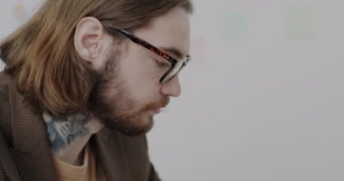 Moda takım elbiseli ve gözlüklü, ofiste dizüstü bilgisayarla çalışan dövmeli bir genç. Modern teknoloji ve kariyer kavramı.