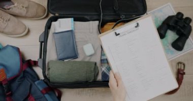 Tatil için bavul hazırlayan pano tıkırdayan seyahat listesiyle kadın elinin yakın çekimi. Turizm ve bagaj hazırlama konsepti.