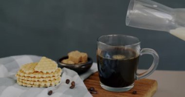 Kahve fincanının yanına, masanın üzerindeki waffle 'ların yanına, gri arka planda süt dökülüyor. Lezzetli tatlı ve tatlı yemek konsepti.