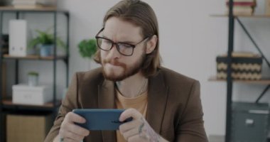 Mobil video oyunu oynayan duygusal genç adam ofisteki akıllı telefonu kullanarak zaferin tadını çıkarıyor. Dövmeli işadamı iş molasında dinleniyor.