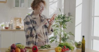 Akıllı telefon kullanan, sosyal medyanın tadını çıkaran ve evde sebze yiyen genç bir kadının portresi. Yaşam tarzı ve aletler konsepti.