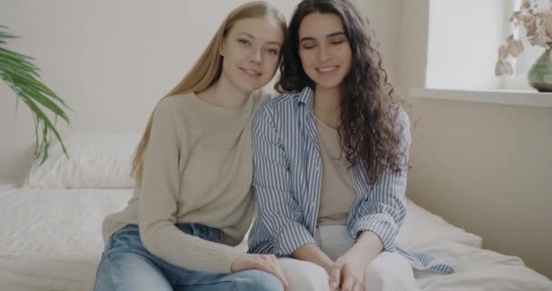 照片上美丽的年轻女性姐妹坐在床上 微笑着看着相机 快乐的家庭和积极的情感概念 — 图库视频影像