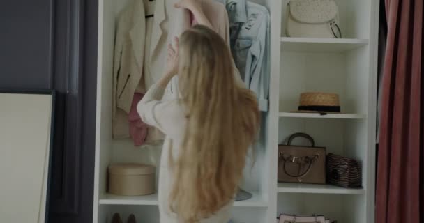 ワードローブの服を見て美しい若い女性は アパート内に立って着用するものを考えている ファッションとスタイルのコンセプト — ストック動画