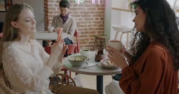 Молодая Женщина Позирует Чашкой Кофе Пока Подруга Фотографирует Смартфоном Кафе — стоковое видео