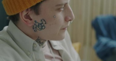 Evinde joystick kullanan neşeli bir adamın yakın plan portresi. Dövmeli ve piercingli moda şapka ve giysiler giyen biri..