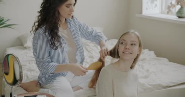気をつけて髪をブラッシングし 自宅で寝室で美容ルーチンを楽しんで話して若い女性 友情と現代のライフスタイルのコンセプト — ストック動画