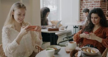 Genç bayan yemek yaparken fotoğraf çekmek için akıllı telefon kullanıyor. Kahve masasında arkadaşlarıyla oturuyor. Modern teknoloji ve fotoğraf konsepti.