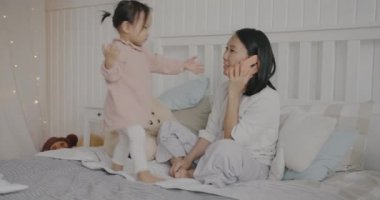 Sevgi dolu bir anne ve küçük kızı cep telefonuyla konuşuyor. Yatak odasında, yatak odasında oturuyor. İletişim ve aile yaşam tarzı kavramı.