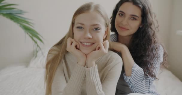 照片上 快乐的金发姑娘和黑发姑娘一起坐在床上 坐在家里 友谊和积极情绪概念 — 图库视频影像