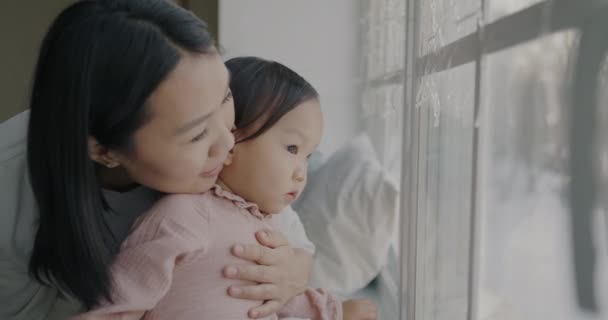 年轻的亚洲女人抱着小女儿 看着窗外 在家里和孩子说话 母亲和儿童概念 — 图库视频影像