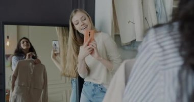 Moda mağazasında arkadaşının modern kıyafetlerle fotoğraf çekerken akıllı telefon kamerası kullanan genç bir bayan. Modern teknoloji ve sosyal medya kavramı.