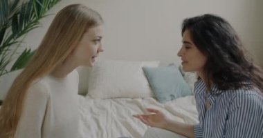 Neşeli arkadaşlar sarışın ve esmer konuşuyorlar ve evde arkadaşlığın tadını çıkarıyorlar. Genç kadınlar yatak odasında oturuyor..