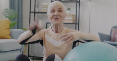 Yaşlı sporcunun portresi çevrimiçi video konuşması yapıyor ve evde fitness topunun yanında el sallıyor. İnsanlar ve iletişim konsepti.