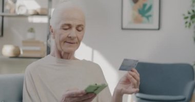 Emekli bir kadının kredi kartıyla ödeme yapması ve akıllı telefon alışverişi yapması. Modern teknoloji ve e-ticaret kavramı.
