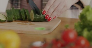 Evdeki mutfakta salatalık doğrayan bıçaklı bir kadın elinin yakın çekimi. Sağlıklı gıda ve beslenme konsepti.