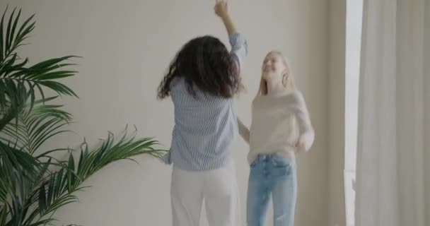 カジュアルな服を着た若い女性の姉妹は ベッドの上で自宅で音楽にダンス笑いジャンプします 友情と肯定的な感情の概念 — ストック動画