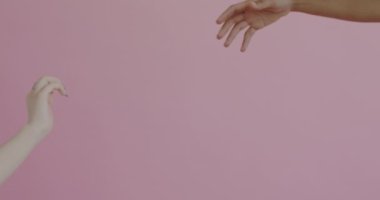 Uzaktan uzanan erkek ve dişinin yakın çekimleri ardından pembe arkaplana dokunuyorlar. Romantik ilişki ve bağlılık kavramı.