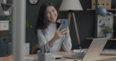 Ofiste iş yerinde eğlenirken akıllı telefon kamerasıyla selfie çeken oyuncu genç bir kadın. Fotoğraf ve aletler kavramı.