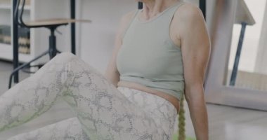 Evde tek başına fiziksel aktiviteye odaklanmış yoga yapan emekli bir kadının eğik portresi. Sağlıklı yaşam tarzı ve sağlık kavramı.