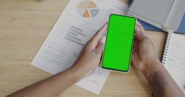 Kadın elinin ve krom tuşlu yeşil ekranlı akıllı telefonun yakın planında iş belgesi var. Girişimci ve aygıt konsepti.