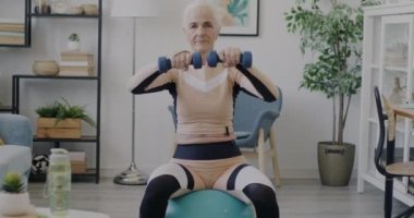 Kıdemli sporcu kadının portresi ağırlık kaldırma eğitimini evde spor salonundaki halterlerle yapıyor. Etkin yaşam tarzı ve emeklilik kavramı.