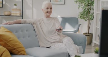 Mutlu, yaşlı bir kadın televizyon seyrediyor. Evde rahat bir koltukta film seyrediyor. Boş zaman konseptinde rahatlama ve olumlu duygu.