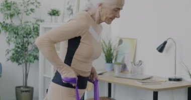 Evde kol kasları gelişen direniş bandıyla yaşlı sporcu kadın eğitiminin portresi. İnsanlar ve fiziksel aktivite kavramı.