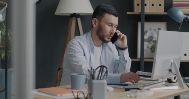コンピュータを操作し オフィスで携帯電話で話す若い出生男の肖像画 専門的な会話と人々の概念 — ストック動画