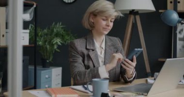 Ofiste akıllı telefon mesajları atan ve gülümseyen neşeli iş kadınının portresi. Modern kablosuz teknoloji ve işyeri konsepti.