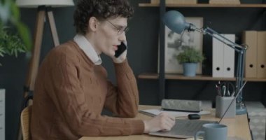 Cep telefonuyla konuşan genç adamın portresi ve ofisteki iş aktivitelerine odaklanmış bir laptop kullanımı. İş ve iletişim konsepti.