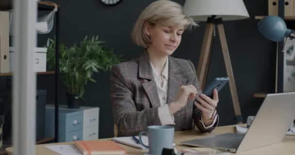 スマートフォンのテキストメッセージを使用して明るいビジネス女性の肖像画やオフィス内で笑顔 現代の無線技術と職場の概念 — ストック動画